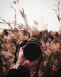 Close-up of hand holding camera against sky