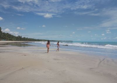 Women walking on shore at beach against sky