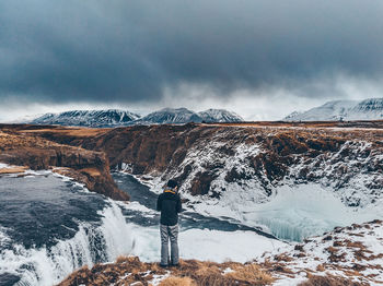 Rear view of person standing on snowcapped mountain against sky