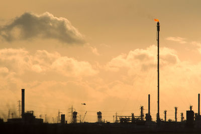 Silhouette factory against sky during sunset