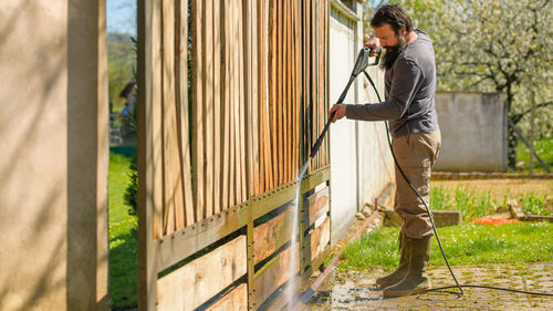 Side view of man cleaning gate in yard