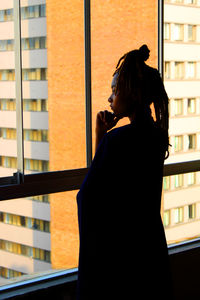 Side view of woman looking through window at home