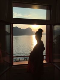 Rear view of silhouette woman looking through window