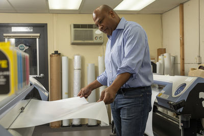 Smiling supervisor putting paper in print machine while working in shop