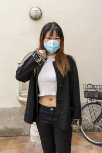 Portrait of woman wearing mask standing against wall