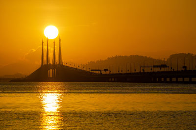 View of bridge over sea against orange sky