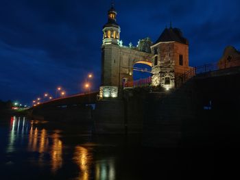 Illuminated buildings by river against sky at night