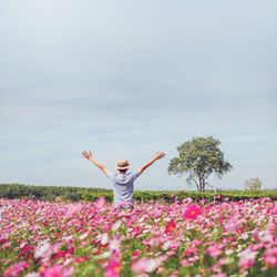 Person standing by flowers on field against sky