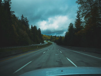 Empty road against cloudy sky seen through car windshield