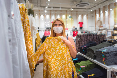 Side view of woman wearing mask looking at clothes at store