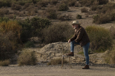 Adult man in cowboy hat with abandoned chair in desert, almeria, spain