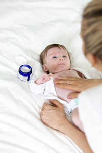 Cropped hand of woman holding cream by son on bed