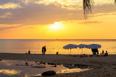 People on beach against sky during sunset