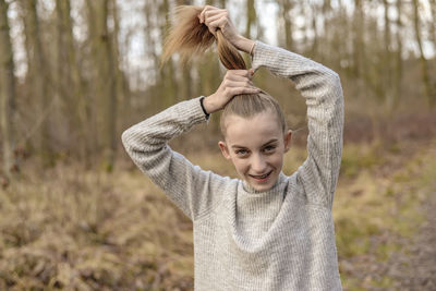 Portrait of smiling teenage girl tying hair in forest