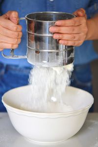 Midsection of woman sifting flour into bowl on table