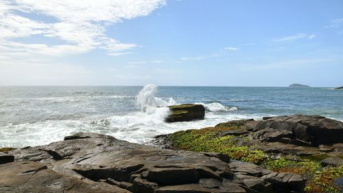 Waves splashing on rocks at shore against sky