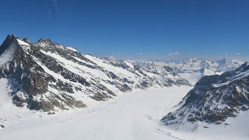 Scenic view of snow covered mountains against clear blue sky