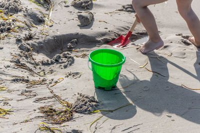 Low section of kid playing on beach with red shovel and green bucket