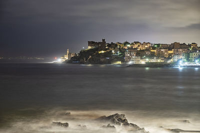 Illuminated buildings by sea against sky at night