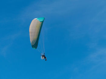 Low angle view of person paragliding against blue sky