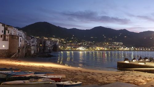 Illuminated city by sea against sky at night