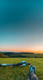 Rear view of man sitting on field against sky during sunset