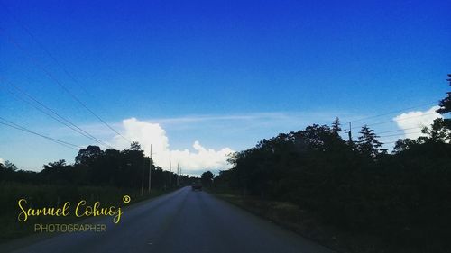 Road amidst trees against blue sky