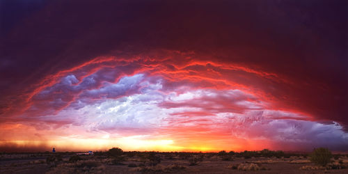 Scenic view of landscape against cloudy sky at sunset