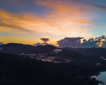 Scenic view of dramatic sky over silhouette mountains during sunset