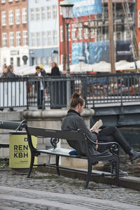 Side view of man sitting on bench in city