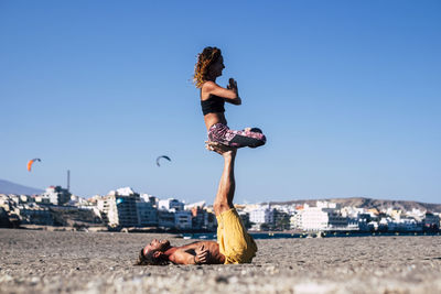 Couple doing yoga at beach against clear sky