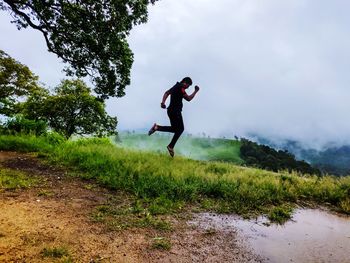 Man levitating over land against sky during foggy weather