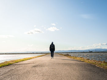 Rear view of man walking on street against sky