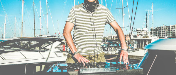Midsection of dj playing music on turntable while standing on yacht