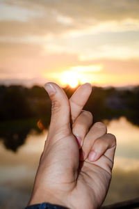 Close-up of human hand against sky during sunset