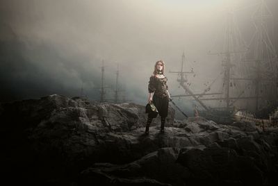 Young woman standing on rock against sky