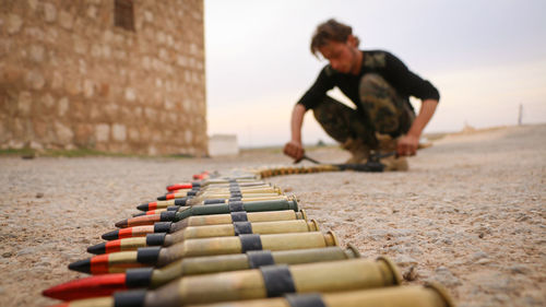 Full length of man arranging bullets on land against sky