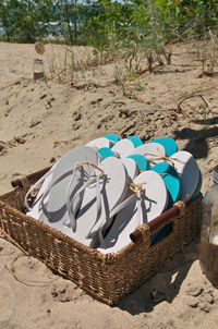 Basket full of pairs of flip flop sandals in white as well as turquoise blue at the beach