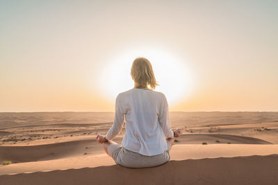 Rear view of woman sitting on sand at beach