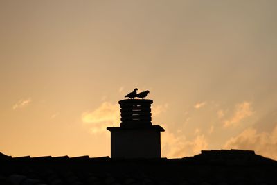 Low angle view of silhouette birds perching on chimney against sky