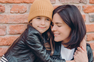 Close-up of girl embracing mother against brick wall