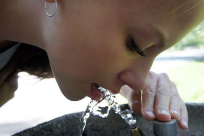 Close-up of young woman drinking water though faucet in park