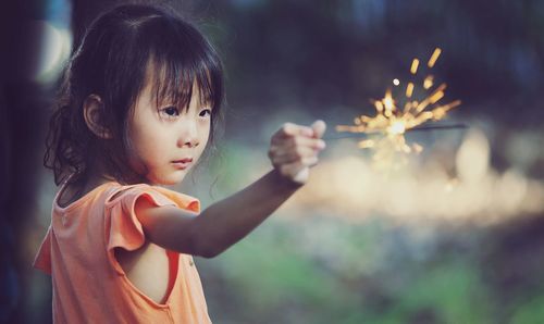 Cute girl holding illuminated sparkler outdoors