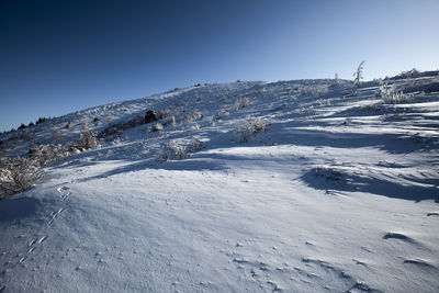 Snow covered landscape against clear blue sky