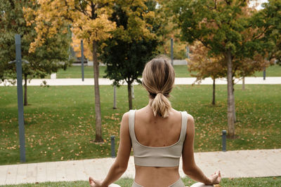 Rear view of woman doing yoga against trees