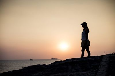 Silhouette man standing on rock by sea against sky during sunset