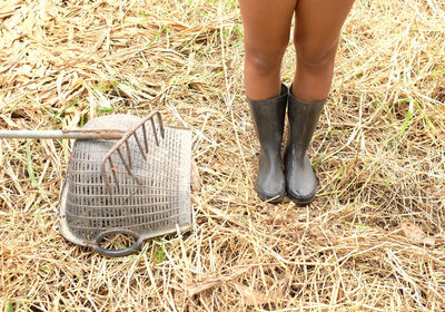 Low section of woman in rubber boot standing by gardening equipment on field