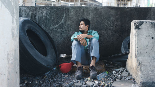 Full length of thoughtful man sitting against wall