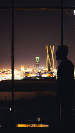Silhouette man standing by glass window at night
