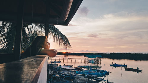 Woman sitting on boat in sea against sky during sunset